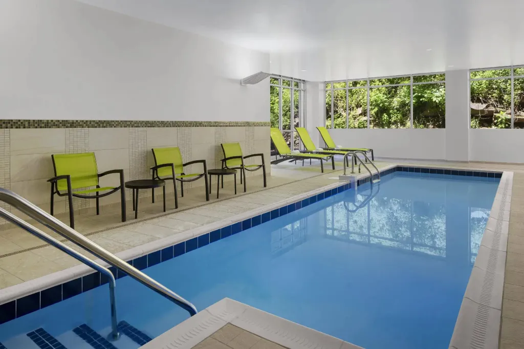 Une piscine interieure avec des transats verts et un mur carrelé.
