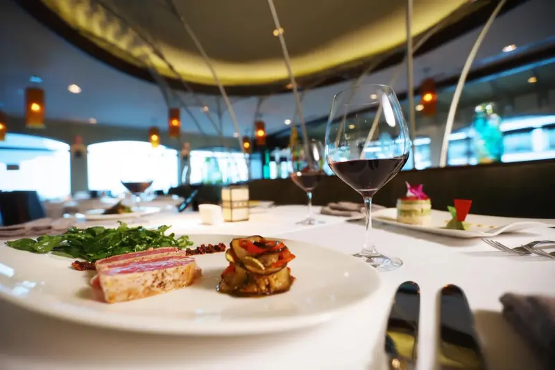 Une table est dressée avec des plats raffinés et des verres de vin dans une salle lumineuse.