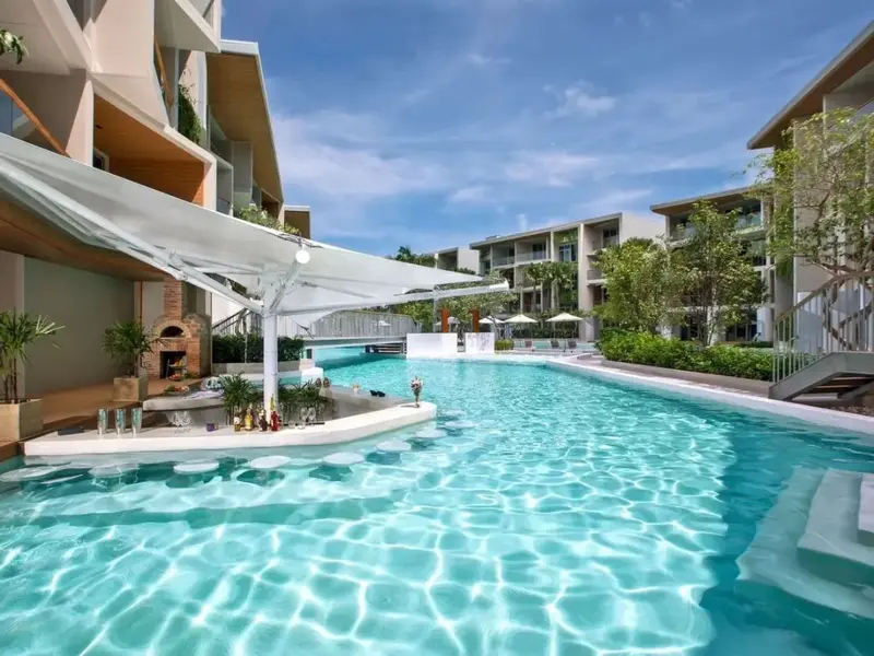 Une piscine turquoise bordée d'un bar ombragé et de bâtiments résidentiels.