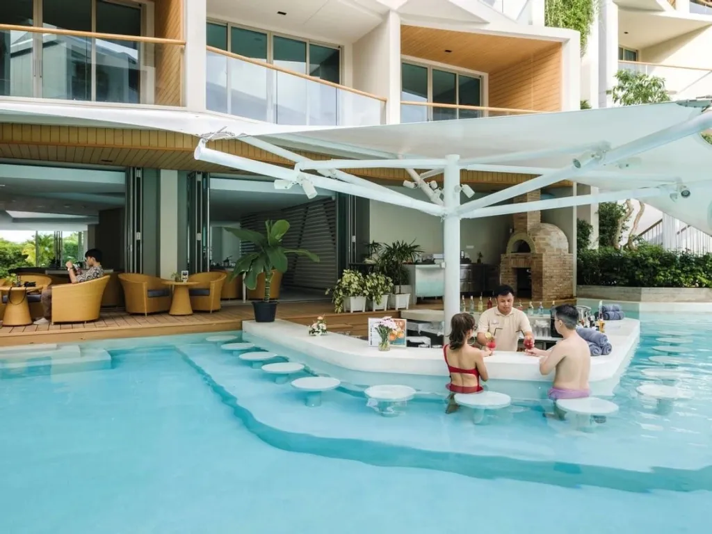 Un bar à cocktails est installé dans une piscine turquoise, avec des clients assis sur des tabourets.