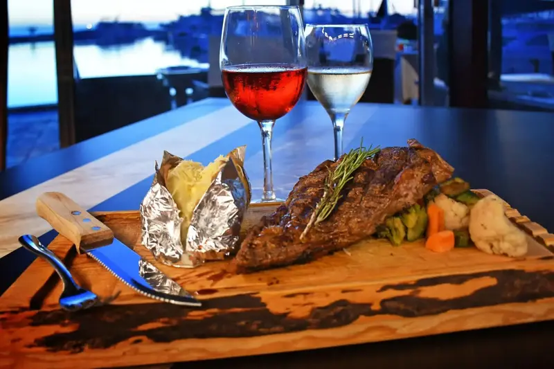 Un plat de viande grillée accompagné de légumes et d'une pomme de terre au four est présenté sur une planche en bois.