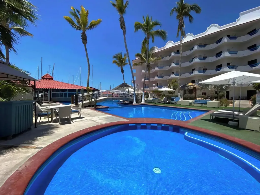 Piscine bleue bordée d'une terrasse ensoleillée avec des transats et des palmiers.