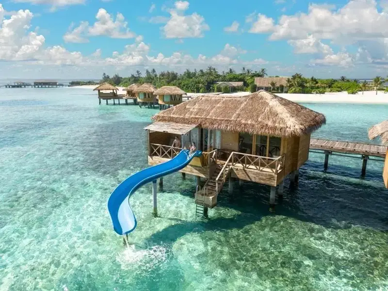 Des bungalows sur pilotis surplombent une eau turquoise et une plage de sable blanc.