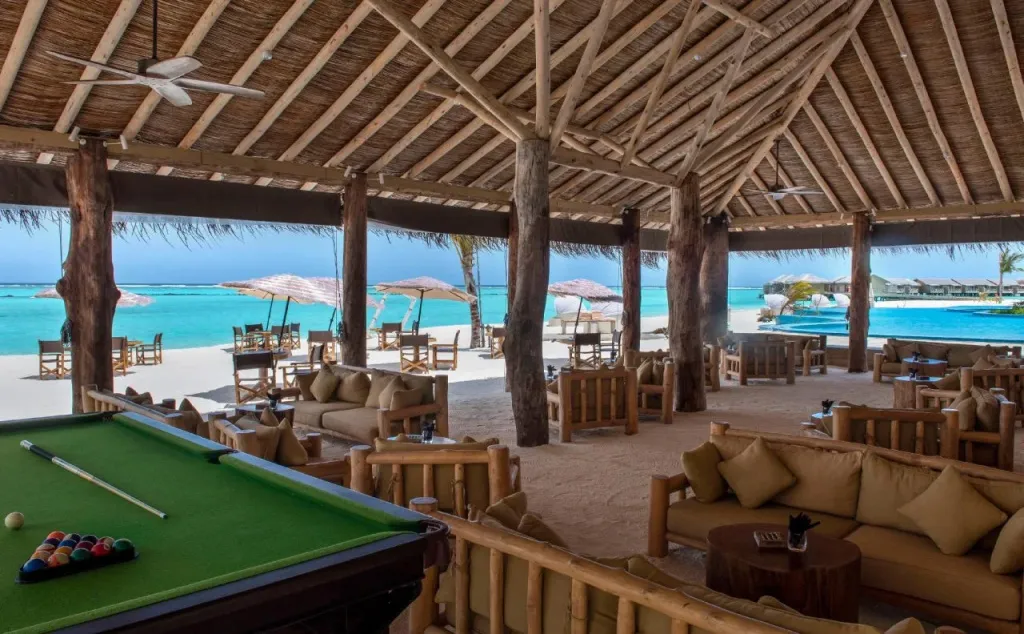 Espace de détente ombragé avec des canapés et des tables donnant sur une plage.