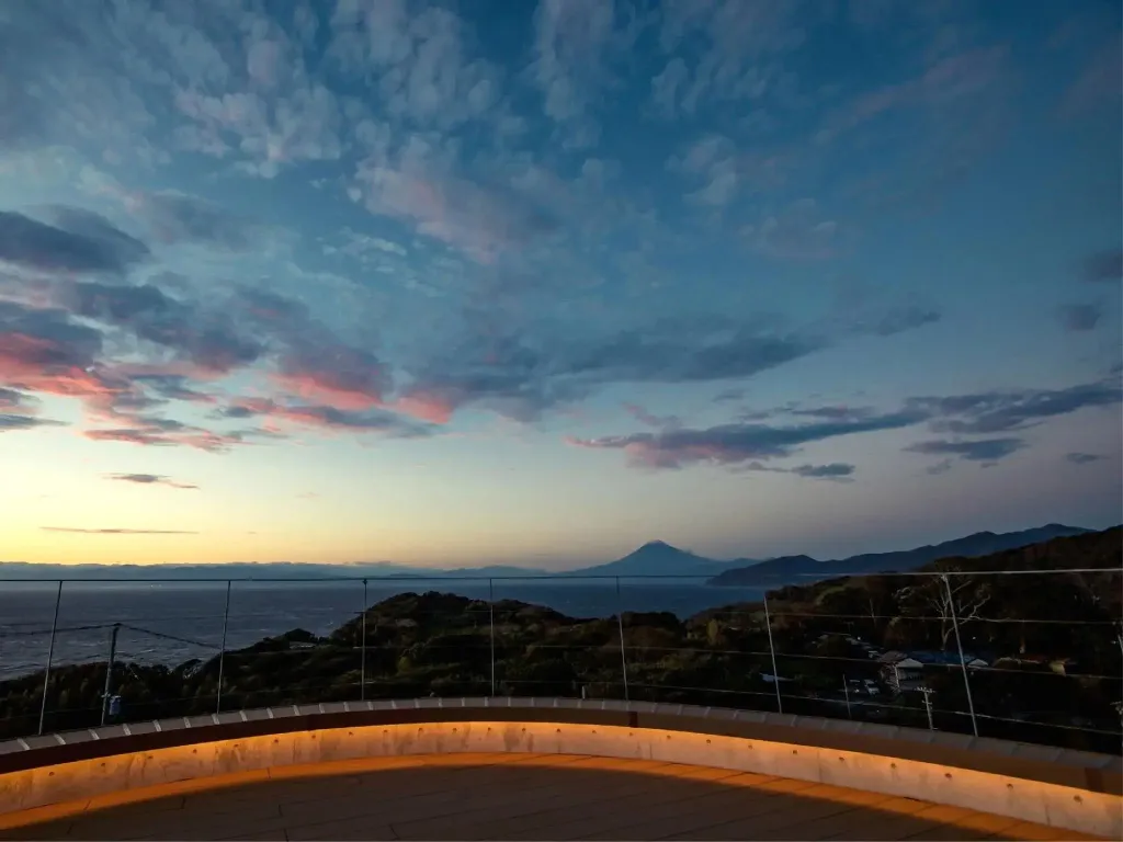 Un ciel nuageux au coucher du soleil surplombe une vue sur la mer et les collines.
