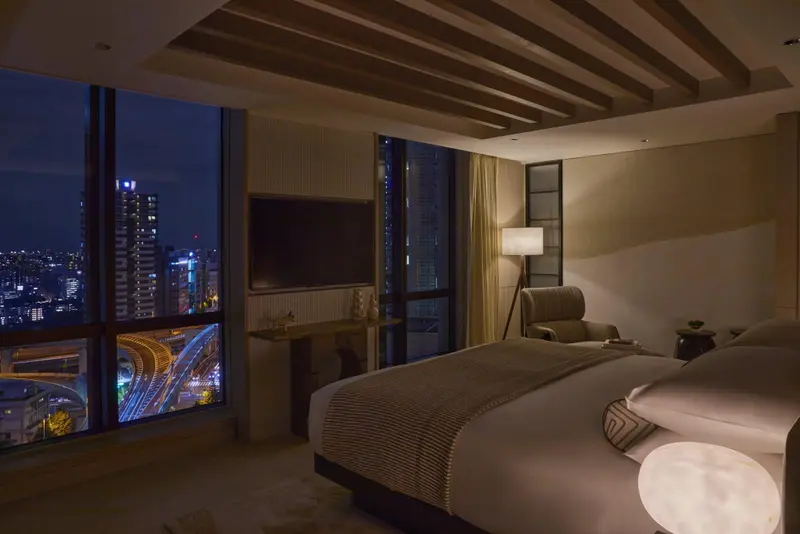 Une chambre moderne avec un grand lit face à une vue nocturne sur la ville.