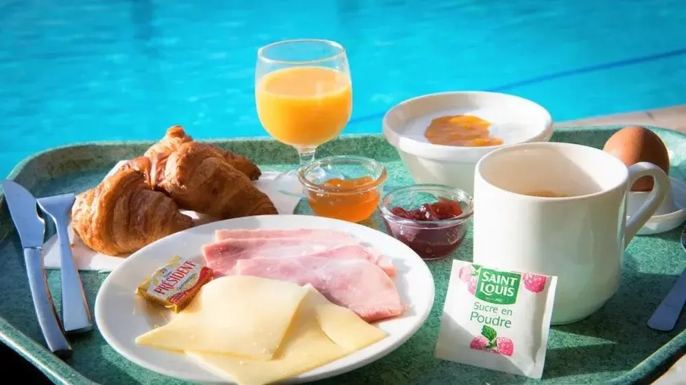 Un plateau de petit-déjeuner avec viennoiseries, jambon, fromage et boissons est présenté en extérieur.