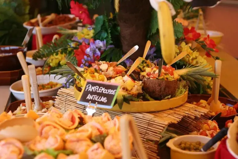 Présentation colorée de plats variés sur un buffet décoré de fleurs et de fruits.