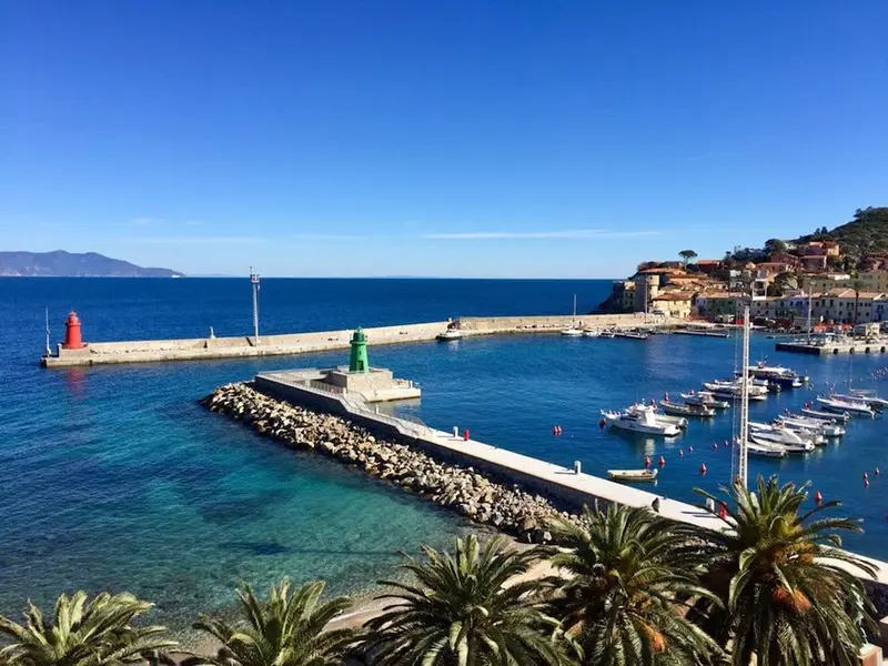Vue aérienne d'un port de plaisance ensoleillé avec des bateaux amarrés et des bâtiments colorés sur une colline.