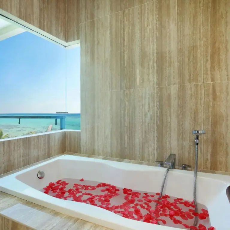 Une baignoire remplie de pétales de roses se trouve dans une salle de bain carrelée avec vue sur la mer.
