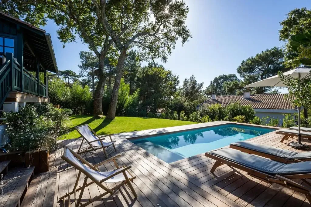 Une piscine rectangulaire bordée d'une terrasse en bois, avec des transats et des chaises longues.