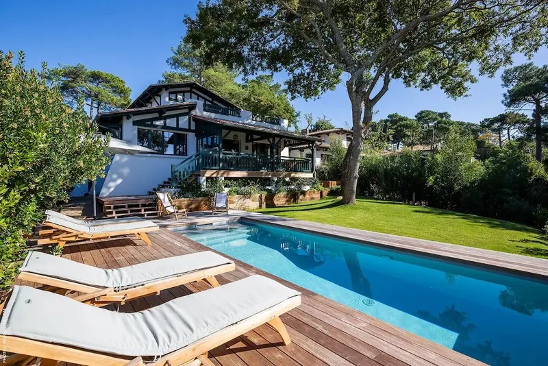 Une piscine bordée de chaises longues devant une maison à l'architecture particulière.