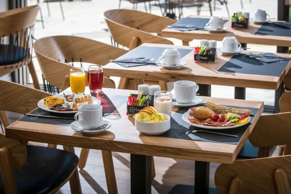 Une table est dressée pour le petit-déjeuner avec des plats variés et des boissons.