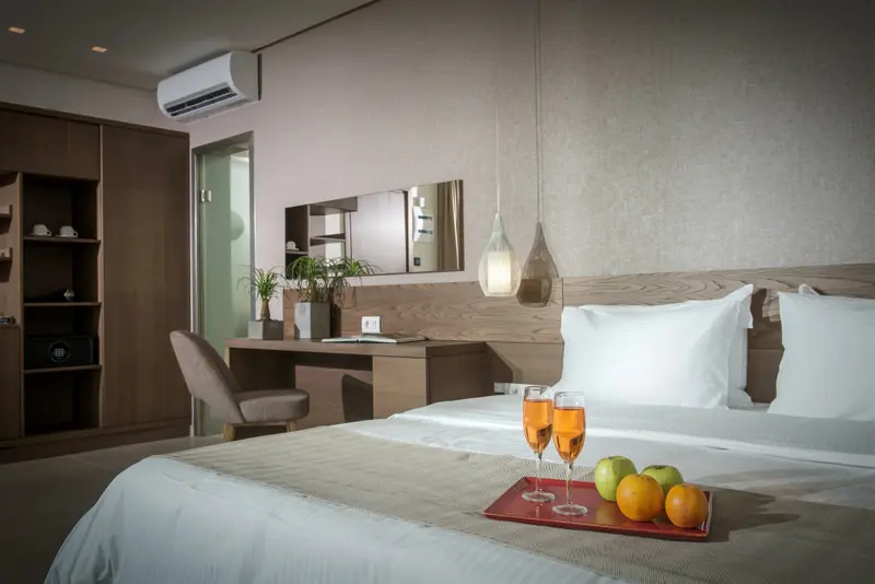 Une chambre lumineuse avec un lit fait et une table de chevet décorée de fruits et de boissons.