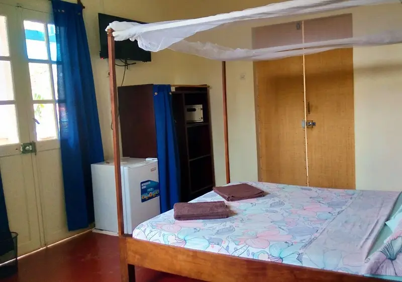 Une chambre lumineuse avec un lit recouvert d'une moustiquaire et un réfrigérateur.