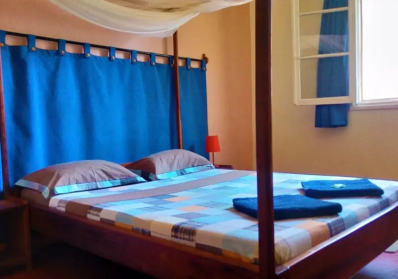 Un lit double avec moustiquaire dans une chambre aux murs orangés.