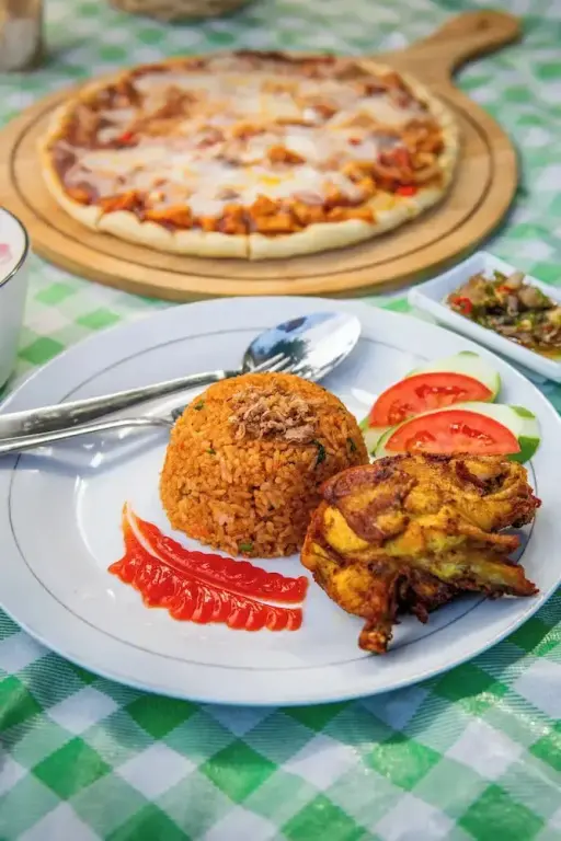 Assiette de riz frit et de poulet grillé avec une pizza en arrière-plan.