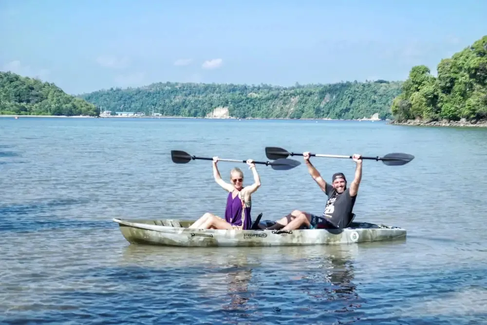 Deux personnes sourient en pagayant sur une eau calme.