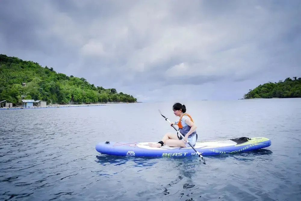 Une personne pratique le paddleboard sur une eau calme, entourée d'îles verdoyantes sous un ciel nuageux.
