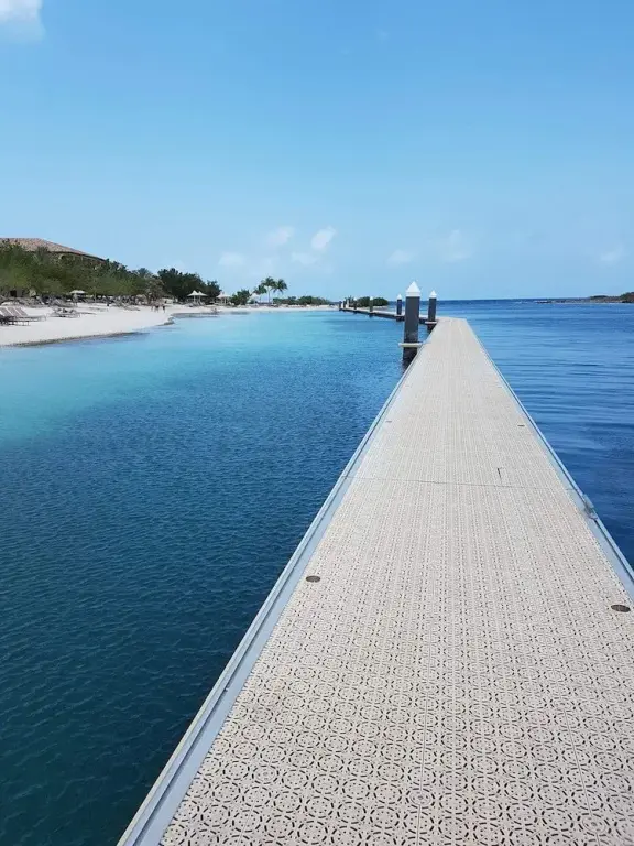 Un long ponton s'avance sur une eau turquoise vers une plage de sable blanc.