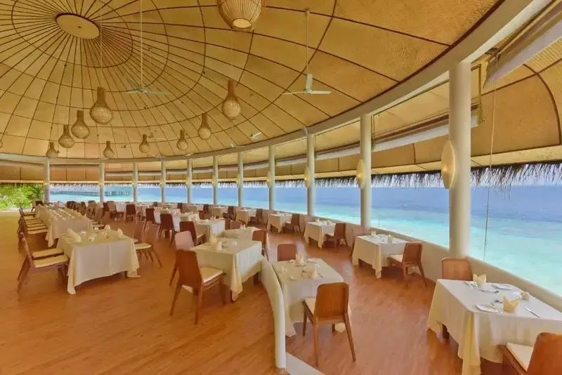 Une salle lumineuse avec de nombreuses tables dressées face à l'océan.