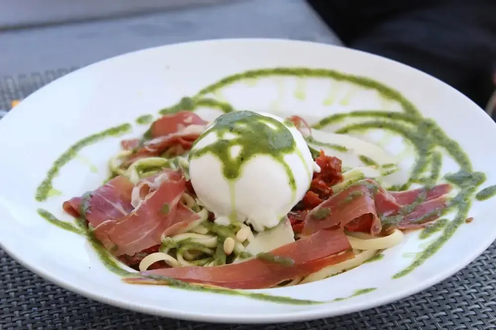 Assiette de pâtes garnie de jambon cru et de fromage frais, nappée d'une sauce verte.