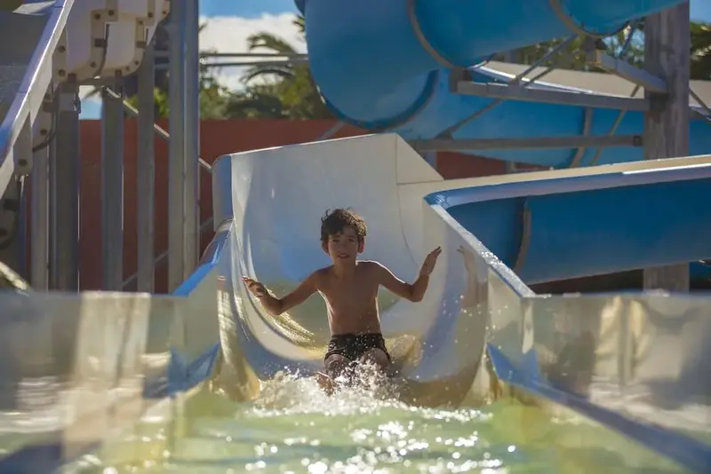 Un enfant glisse dans un toboggan aquatique en plein soleil.