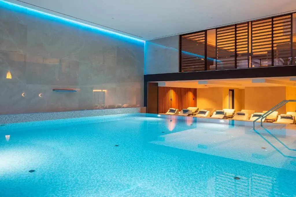 Une piscine intérieure lumineuse avec des transats alignés sur une mezzanine.