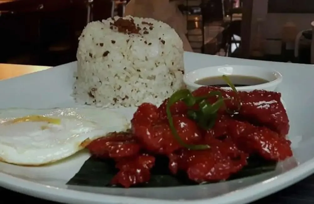 Assiette de riz, d'œuf au plat et de viande rouge nappée d'une sauce.