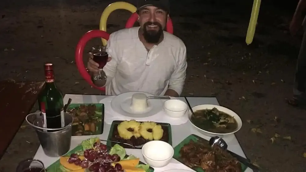 Un homme souriant est assis à une table garnie de plats et de boissons.