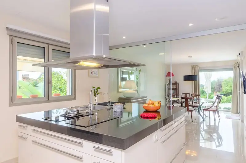 Une cuisine moderne avec un îlot central et une vue sur une salle à manger lumineuse.