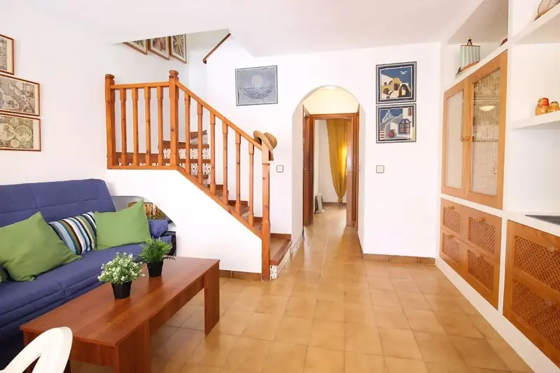 Un salon lumineux s'ouvre sur un couloir et un escalier en bois.