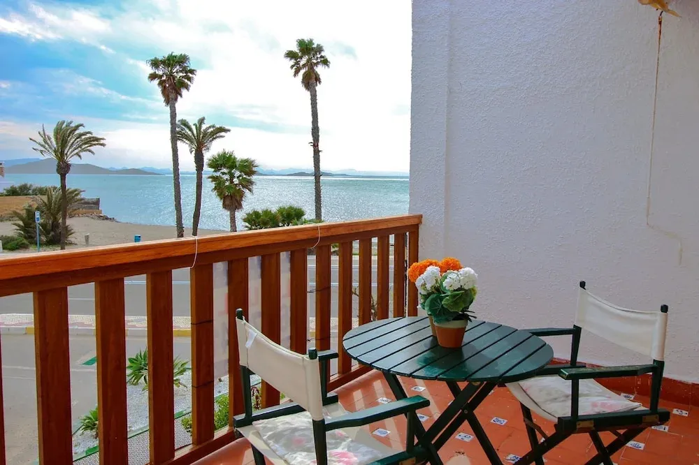 Une petite table et des chaises se trouvent sur un balcon avec vue sur la mer et des palmiers.