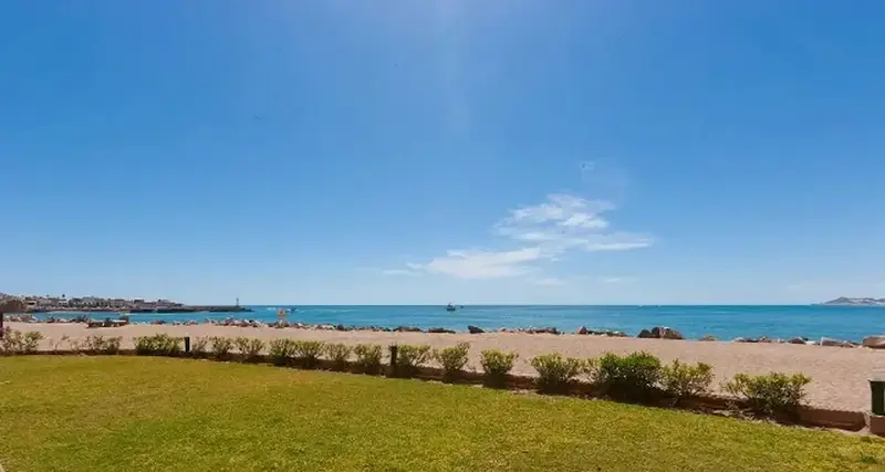 Une plage de sable fin bordée d'une pelouse verte sous un ciel bleu dégagé.