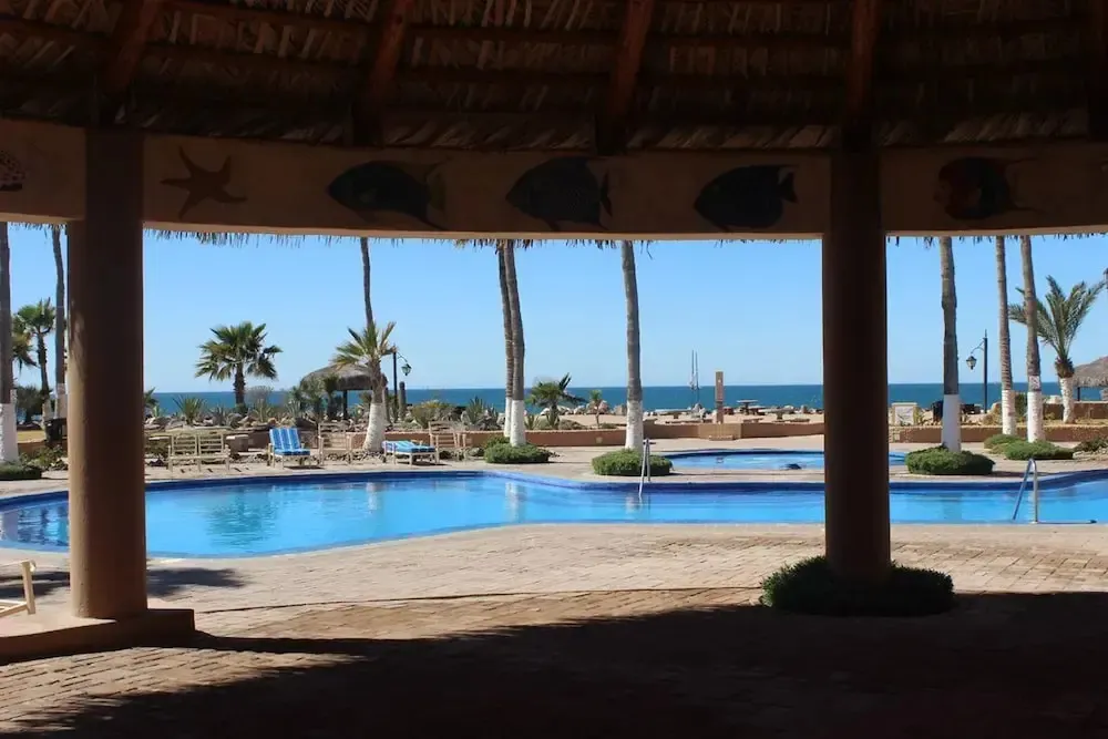 Une piscine bleue bordée de palmiers offre une vue sur la mer et le ciel bleu.