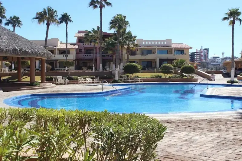 Piscine bleue bordée d'une terrasse ensoleillée devant un bâtiment aux couleurs vives.