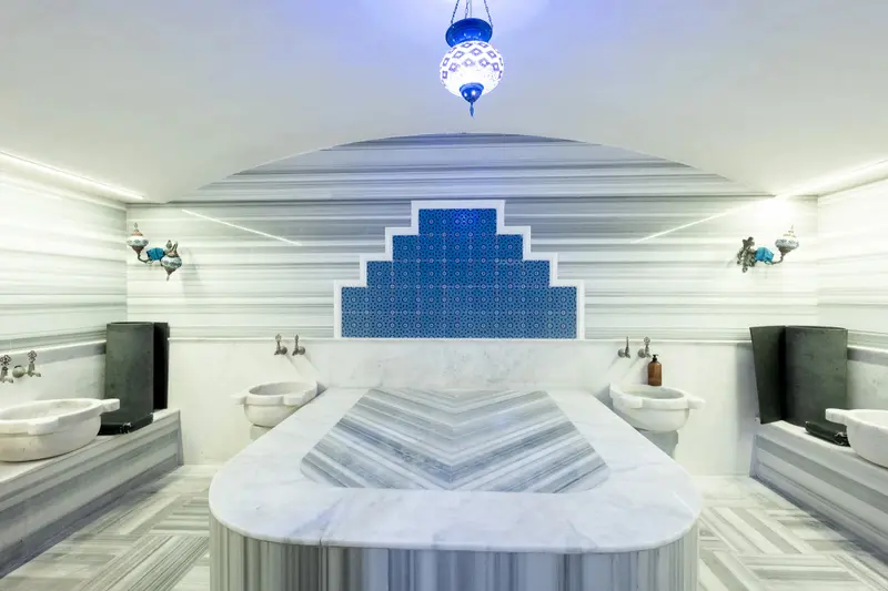 Interieur lumineux avec un grand bassin central en marbre et des lavabos en pierre.