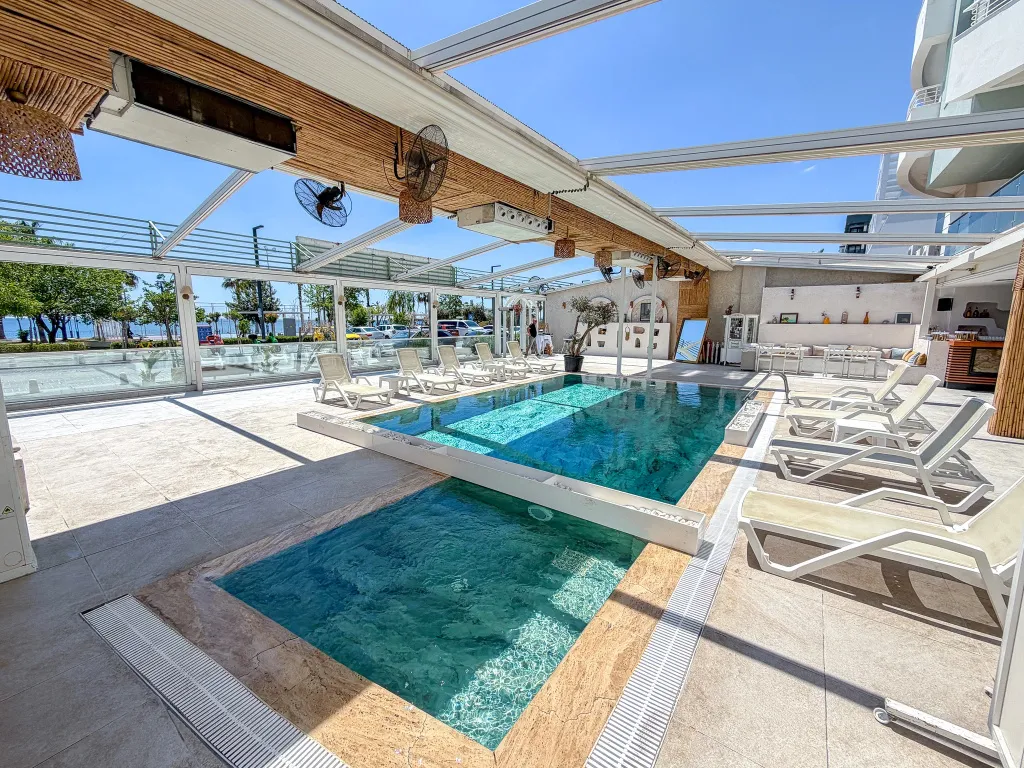 Une piscine rectangulaire avec des transats blancs sous une structure ajourée.