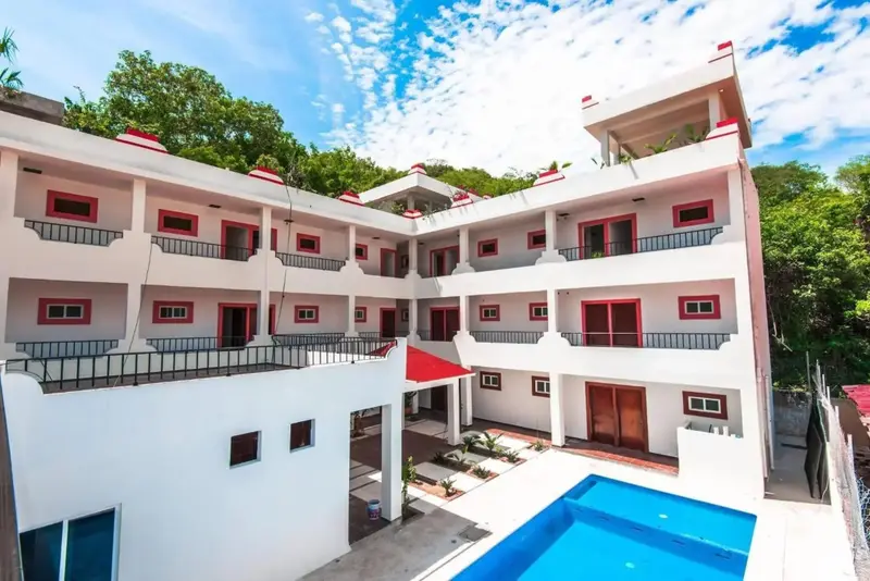 Bâtiment blanc à plusieurs étages avec des balcons et une piscine au premier plan.