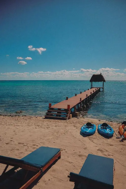 Transats sur une plage de sable fin avec un ponton en bois s'avançant vers la mer.