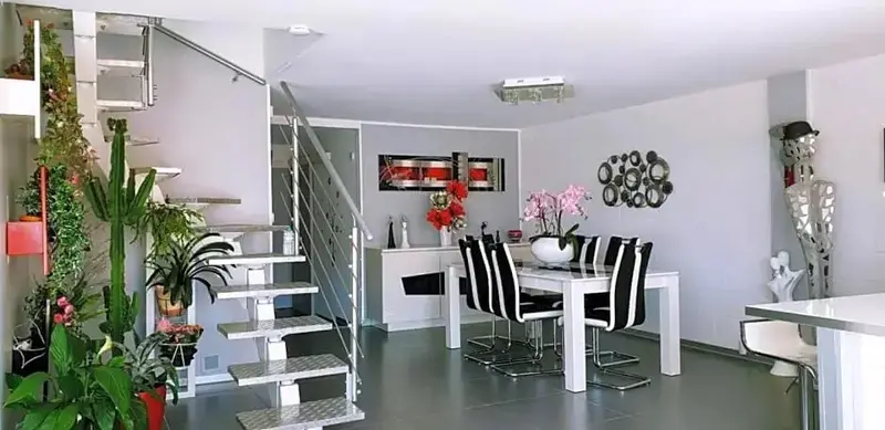 Un espace de vie lumineux avec un escalier métallique et une table à manger.