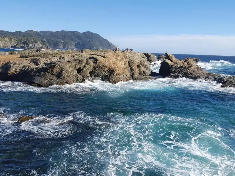Cote rocheuse battue par les vagues sous un ciel bleu.