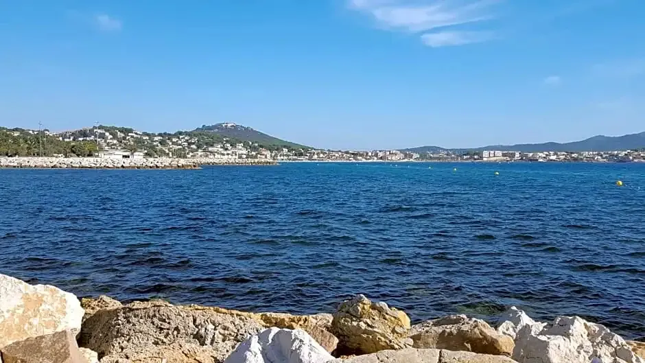 Vue d'une côte rocheuse face à une ville en bord de mer sous un ciel bleu.