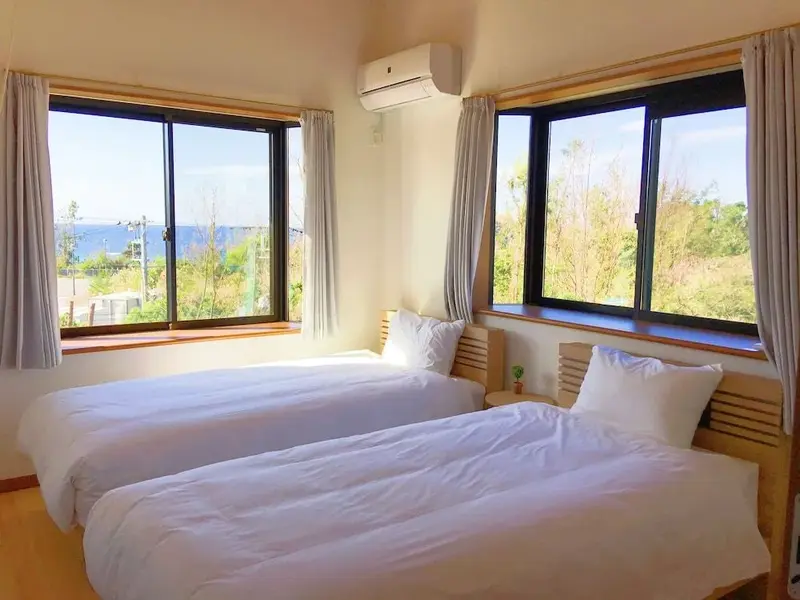 Chambre lumineuse avec deux lits simples et vue sur la mer.