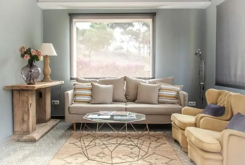 Un salon clair avec un canapé et des fauteuils face à une fenêtre.