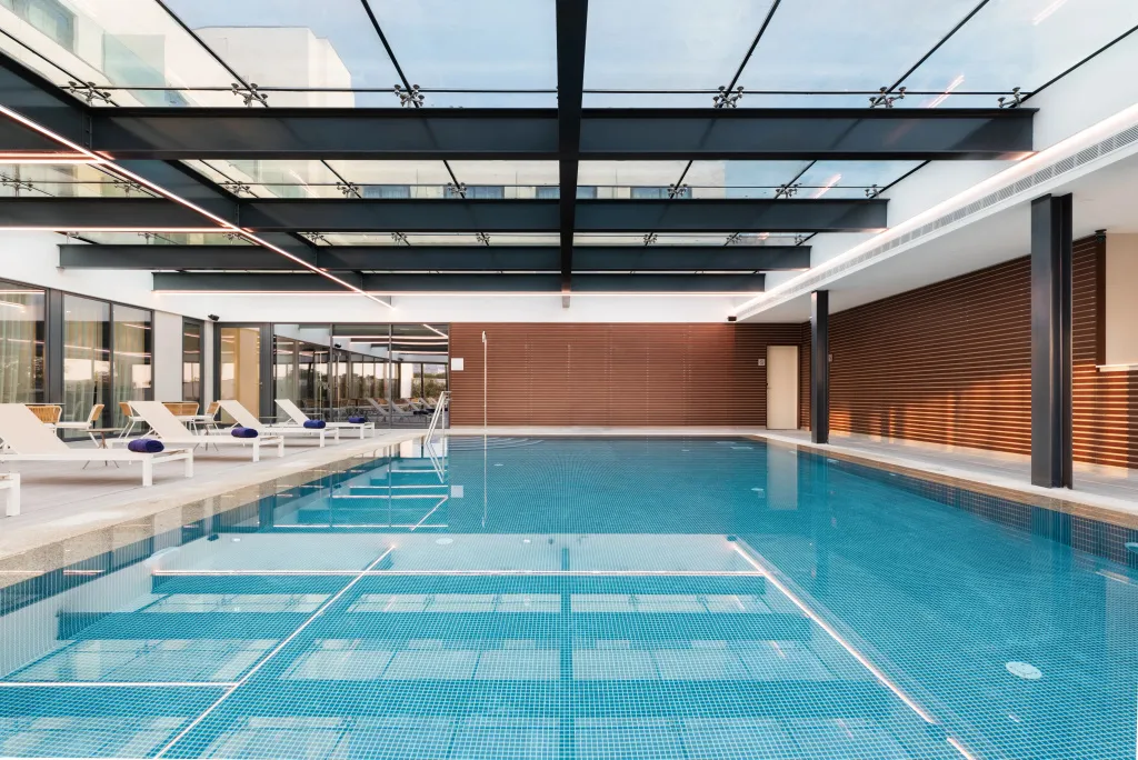Une piscine interieure lumineuse avec des transats blancs.