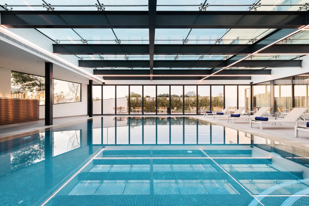 Une piscine intérieure lumineuse avec des transats alignés près de larges baies vitrées.
