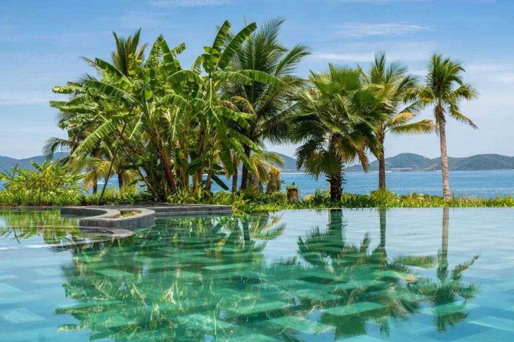Une piscine turquoise reflète la végétation luxuriante et la mer bleue.