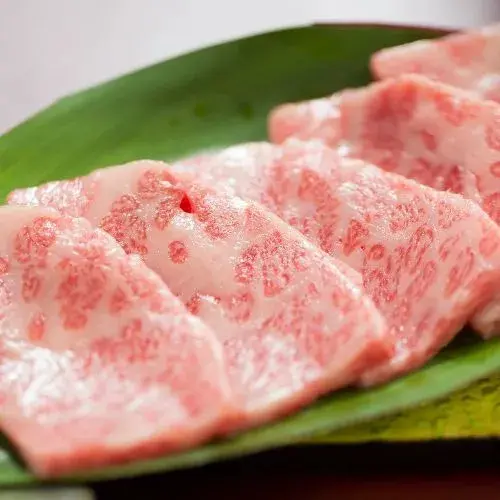 Tranches de viande rosées disposées sur des feuilles vertes.