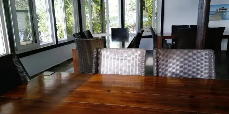 Une grande table en bois est entourée de chaises en osier dans une salle lumineuse.